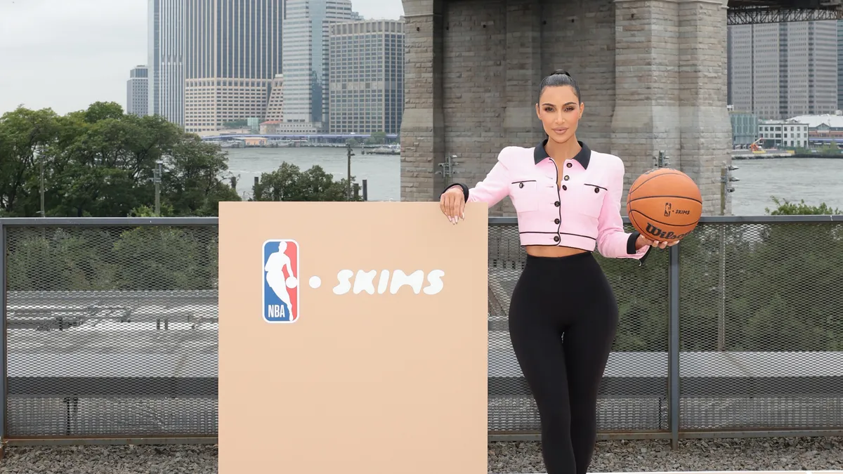 Kim Kardashian standing next to an NBA podium holding a basketball.