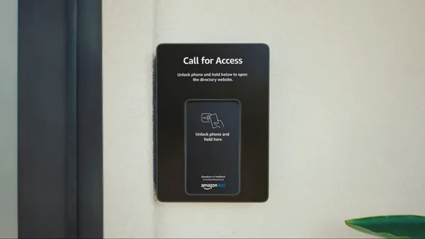 A black panel on a wall that reads "Call for Access - Open phone and hold below to open the directory website." The Amazon Key logo is on the bottom of the panel.