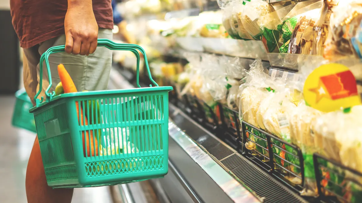 Person choosing fruits and vegetables in basket at supermarket.