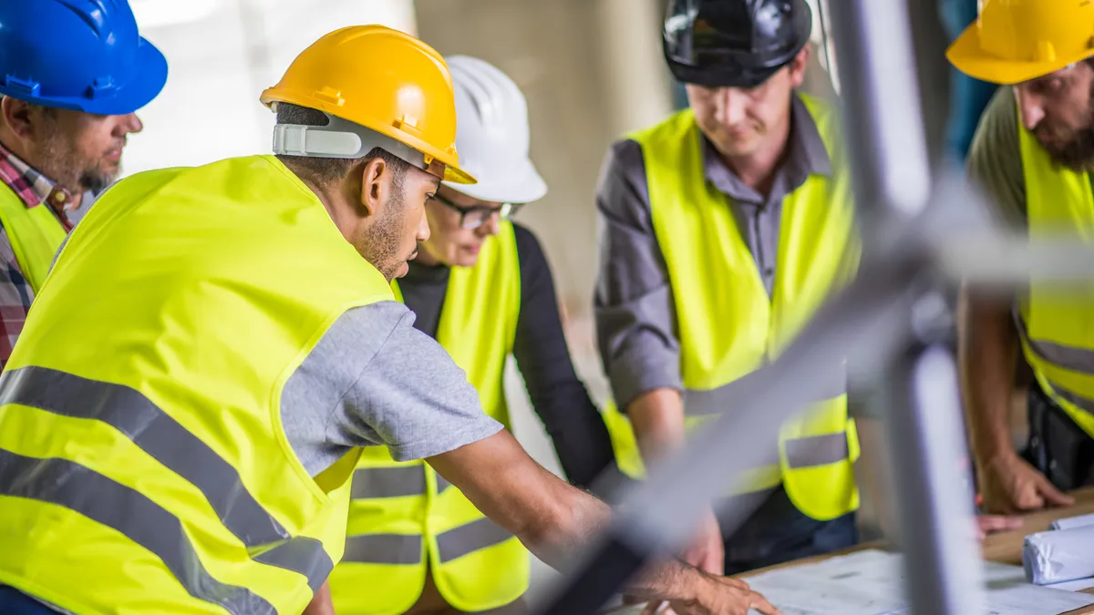 A group of construction professionals discuss plans on a jobsite.