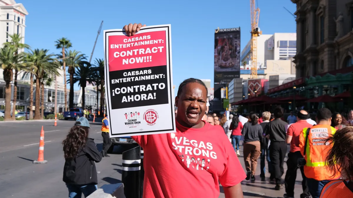 A worker in a red shirt holds a sign that reads "Contract Now!".