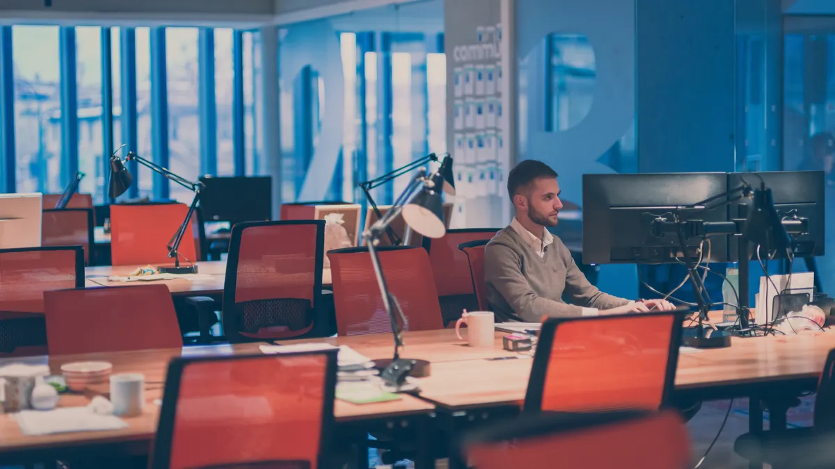 Young businessman working alone at his desk on desktop computer in an open space modern coworking office.