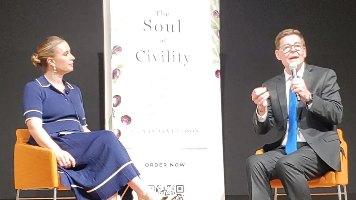 Two people sitting in chairs on a stage in front of sign with book cover that says "The Soul of Civility."
