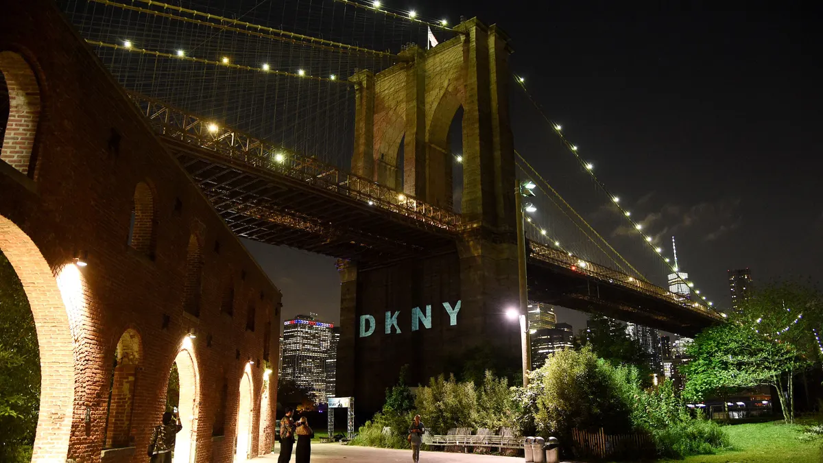 The brand logo for DKNY is projected onto one of the supports for NY's Brooklyn Bridge at night.