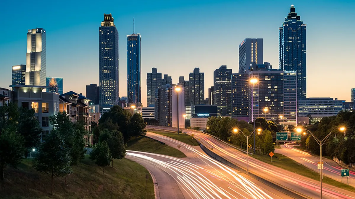 A nighttime view of a city skyline, with streaks of light from the highway in the foreground.