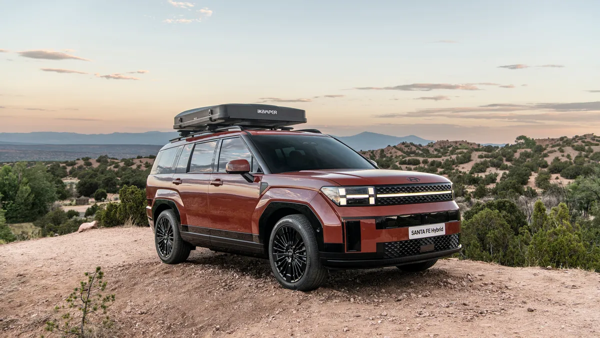 A red 2024 Hyundai Santa Fe hybrid SUV pictured on a dirt trail with desert terrain in the background.