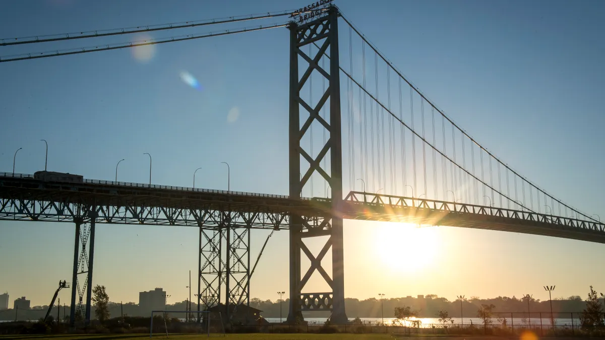 A truck travels across a bridge as the sun sets behind the bridge.