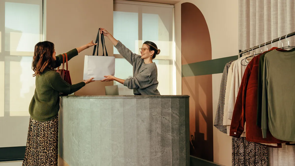 Cheerful clothing store owner handing a customer a shopping bag with clothing items