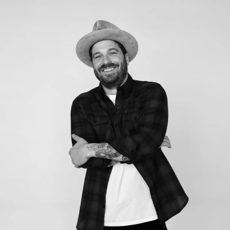 A black-and-white photo shows a smiling man wearing a hat.