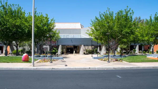 A building sits in the center of the frame on a bright day with trees and foliage out front.