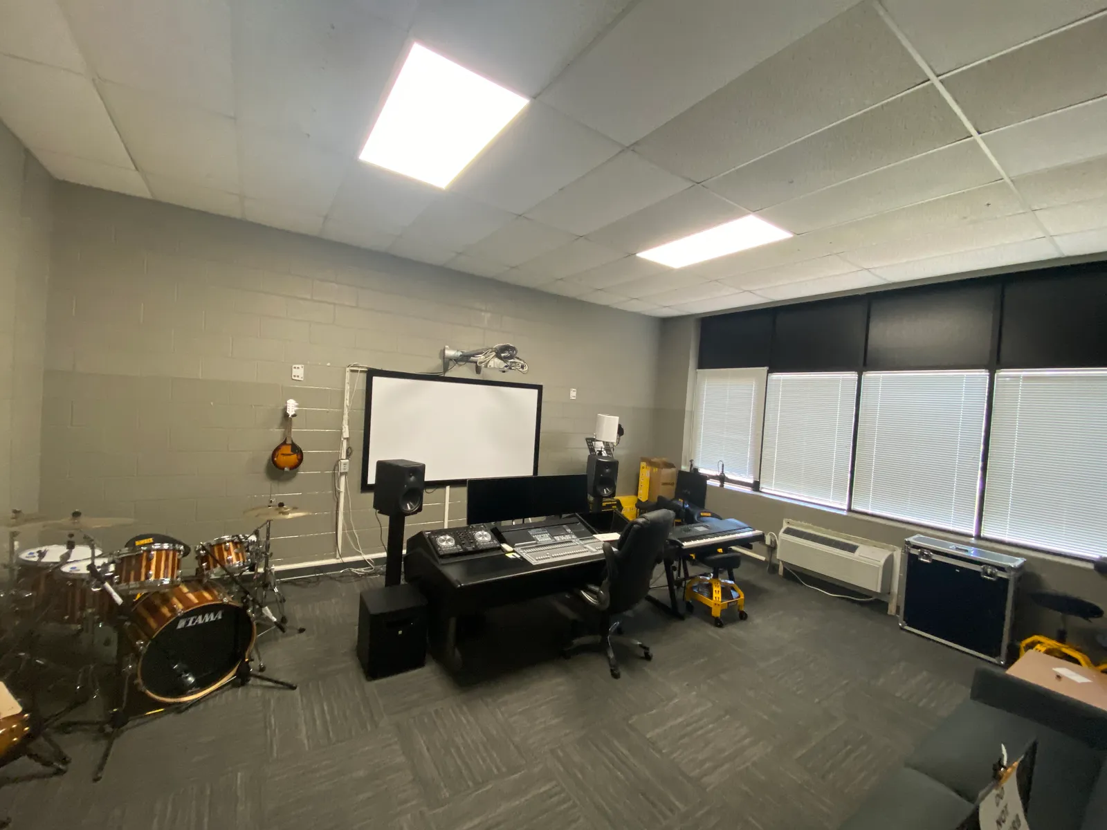 A room has recording equipment, such as a control panel on a table, a screen, a keyboard, and other musical instruments.