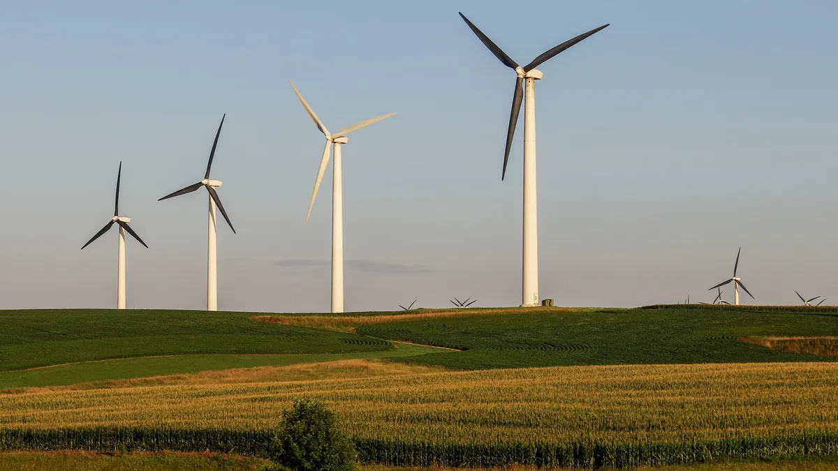 A row of wind turbines in a farm field.