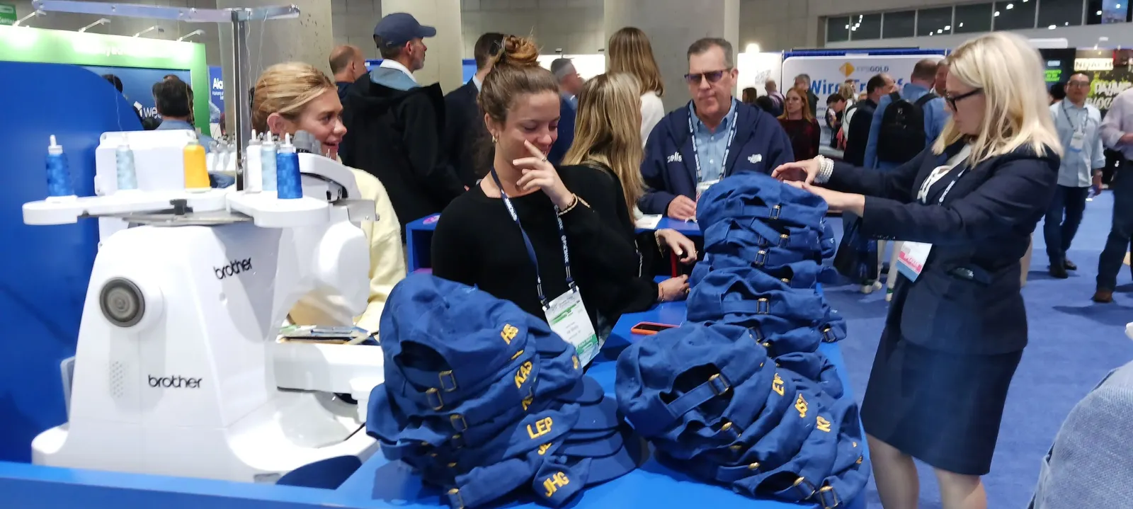 A trade floor booth with people at a sewing maching stitching baseball caps.