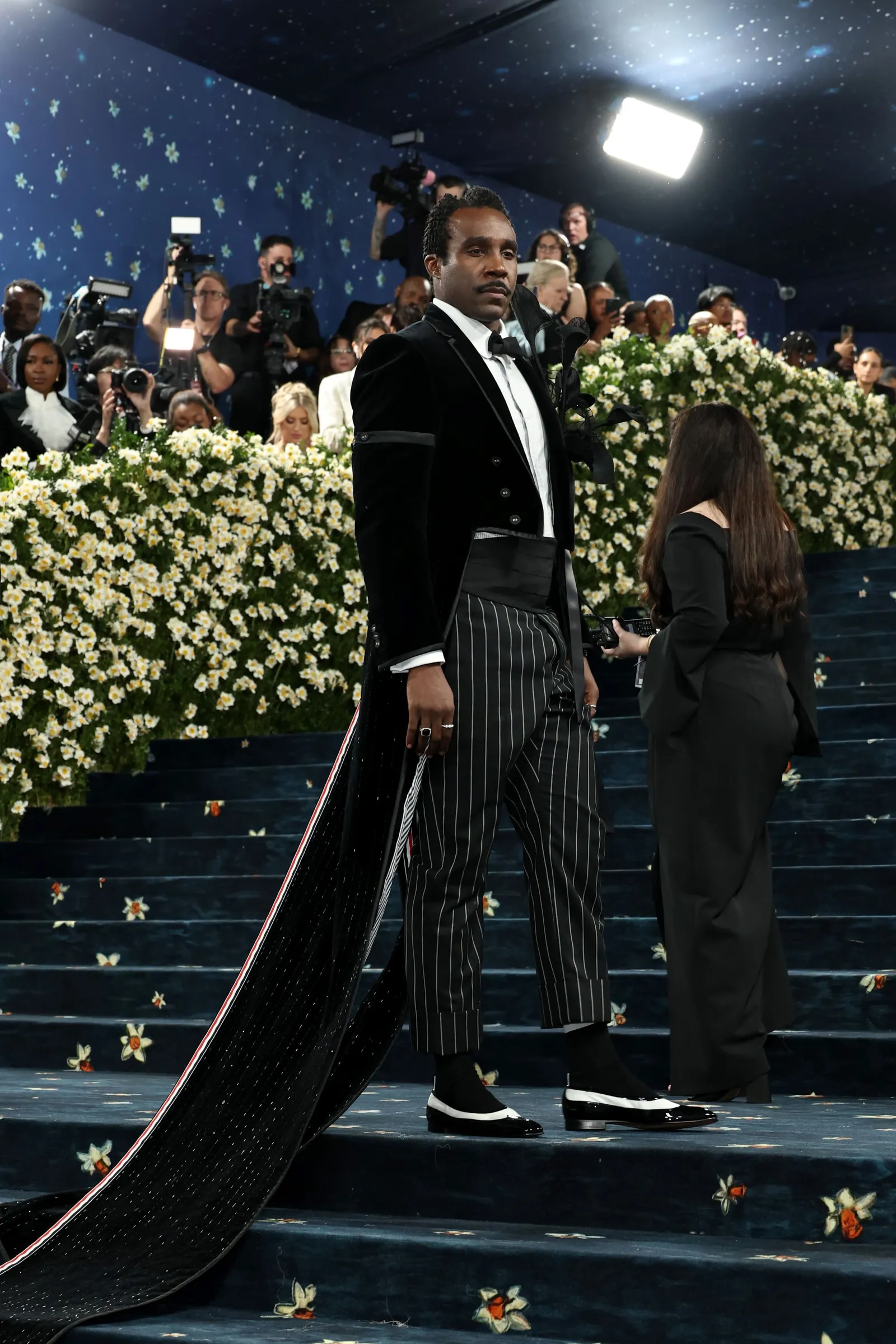 A man in pinstripe pants and long tails stands on a blue staircase.
