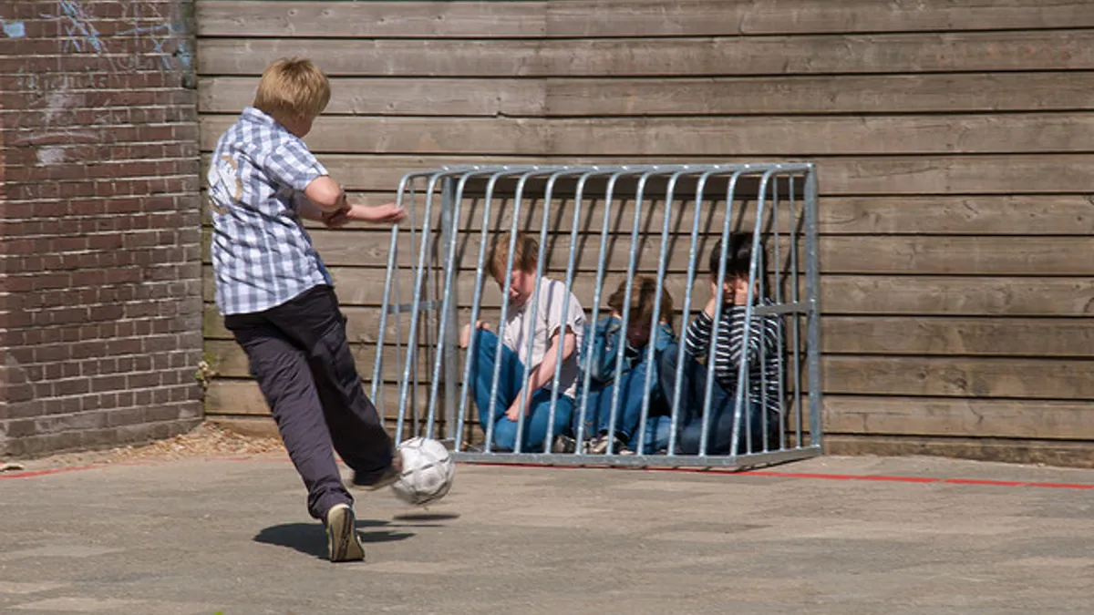 School bully kicking ball at other kids trapped in metal soccer goal.