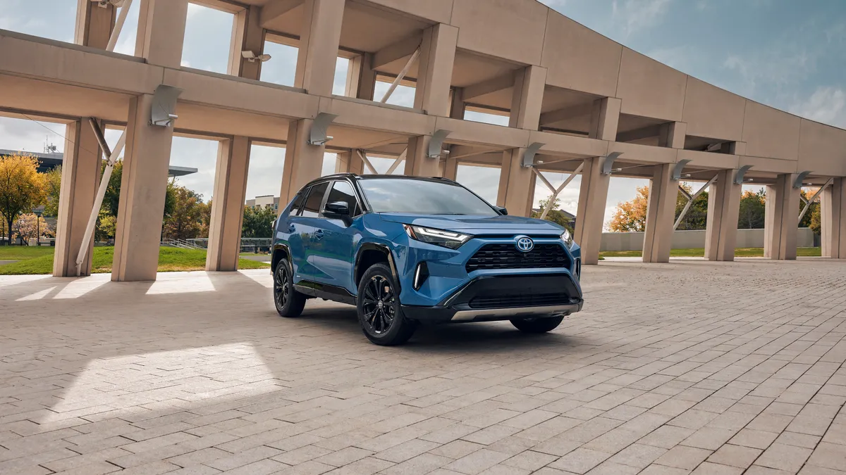 A blue 2024 Toyota RAV4 hybrid SUV parked outside with a concrete building structure in the background.