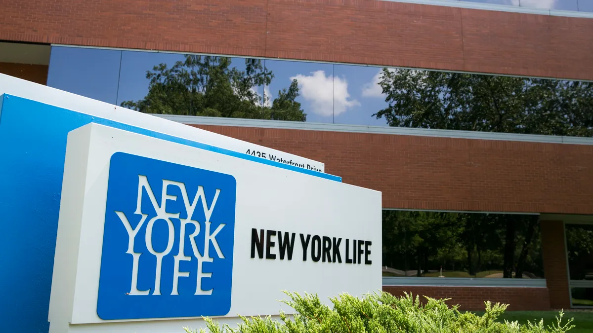 A New York Life corporate logo sign outside an office park with vegetation in the foreground.