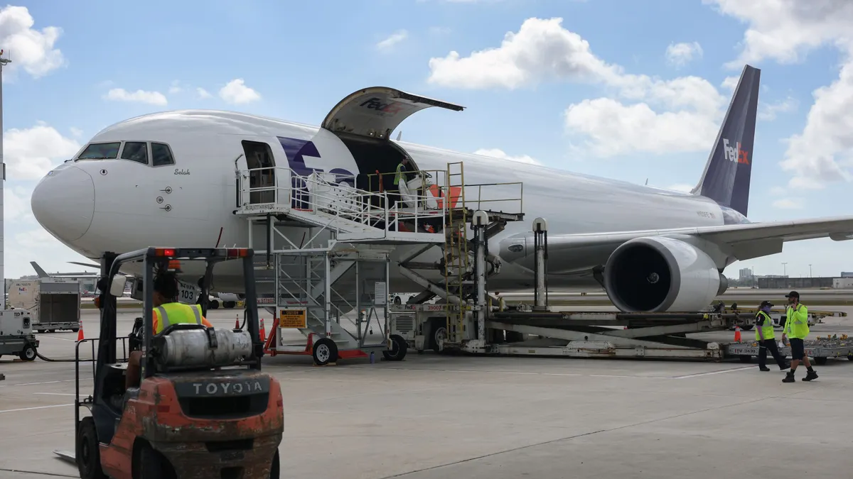 A person drives a forklift in front of a cargo airplane that is being loaded.