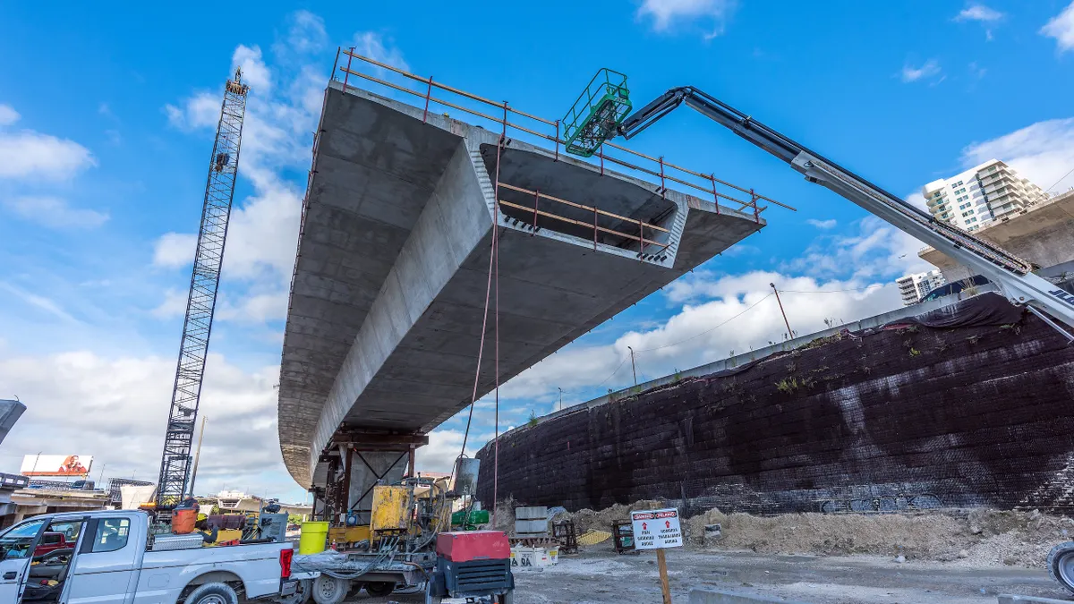 People wearing vests and hard hats standing under a partially finished concrete overpass.