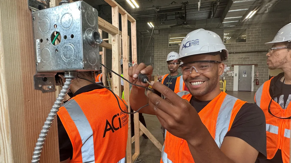 A worker in a hard hat and vest smiles as they work.