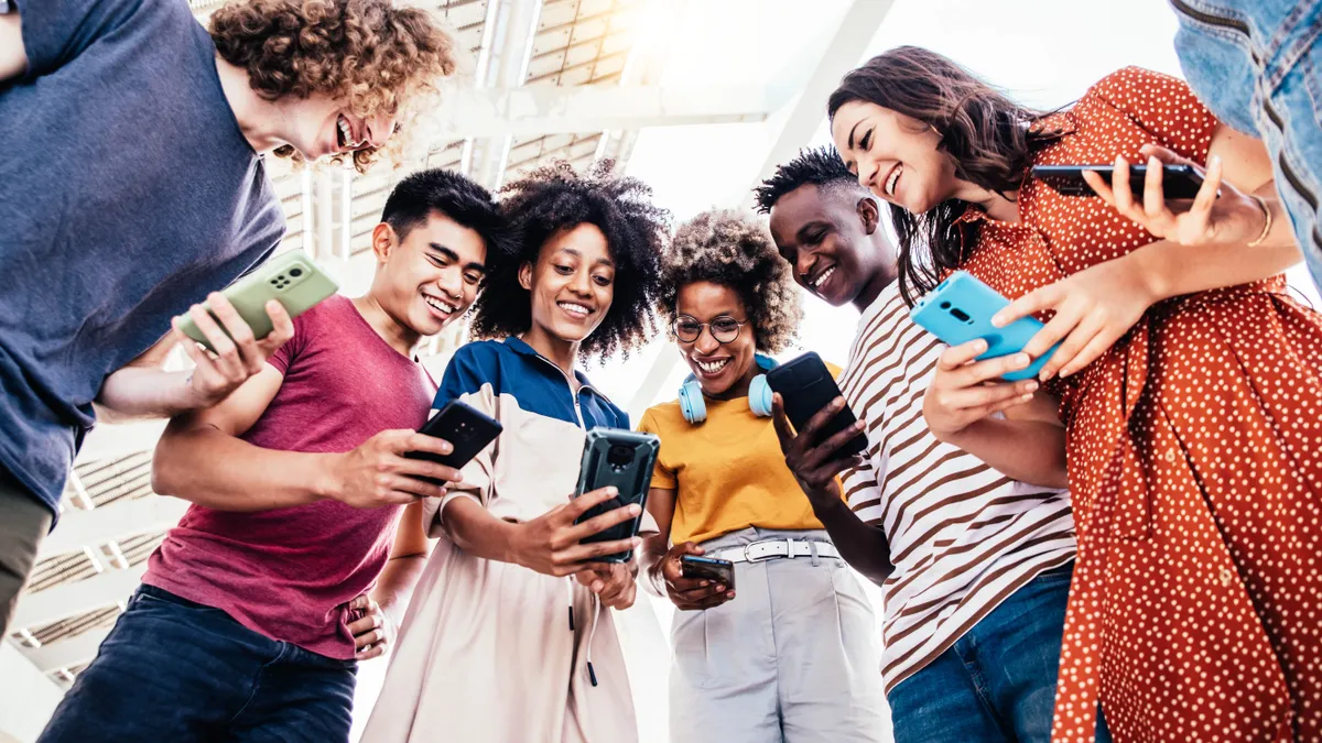 Diverse teenage students using digital smart phones mobile at college campus.