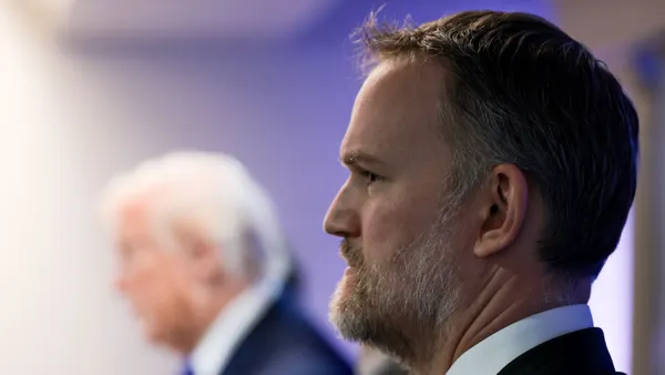 U.S. Trade Representative Jamieson Greer stands in the foreground while President Donald Trump delivers remarks in the background.