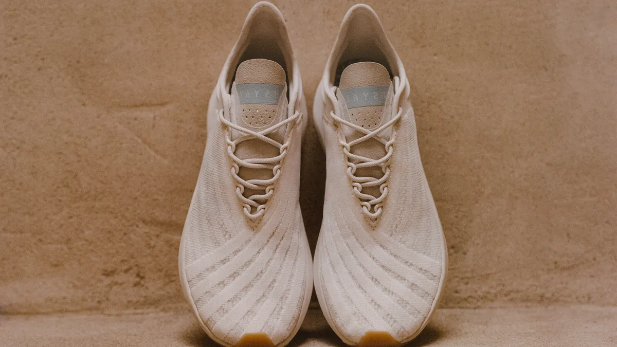 A pair of cream color athletic shoes is propped up on a neutral color wall.