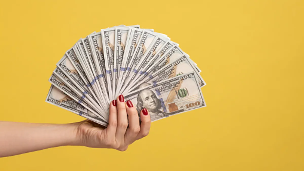 Hand holding money against a yellow background