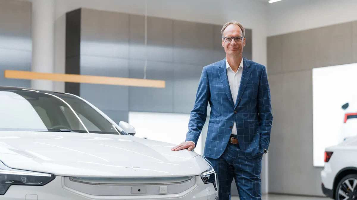 Polestar CEO Michael Lohscheller posing with a white Polestar electric vehicle.