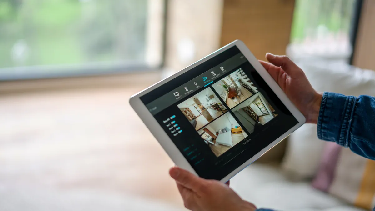 Close-up on a woman monitoring all the rooms in her house with a home security system using a digital tablet.