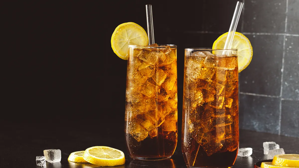 Two glasses of a brown drink with lemons hanging on the side of the glass