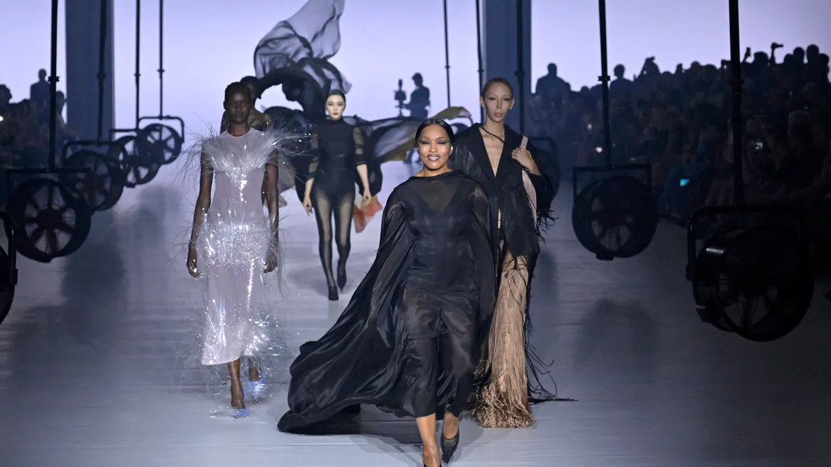 Models wear flowy dresses in black and white and walk down the runway.