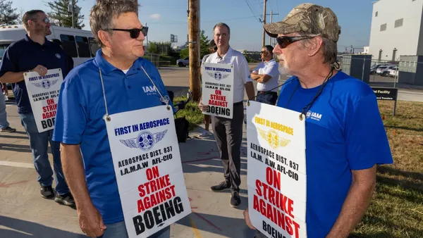 Two men in blue shirts holding signs that say, Strike against Boeing.