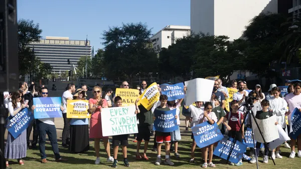 A group of students and adults are standing outside and are holding posters with wording.