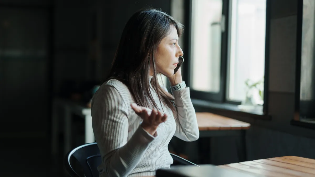 A woman makes a phone call while sitting at a table and gesturing