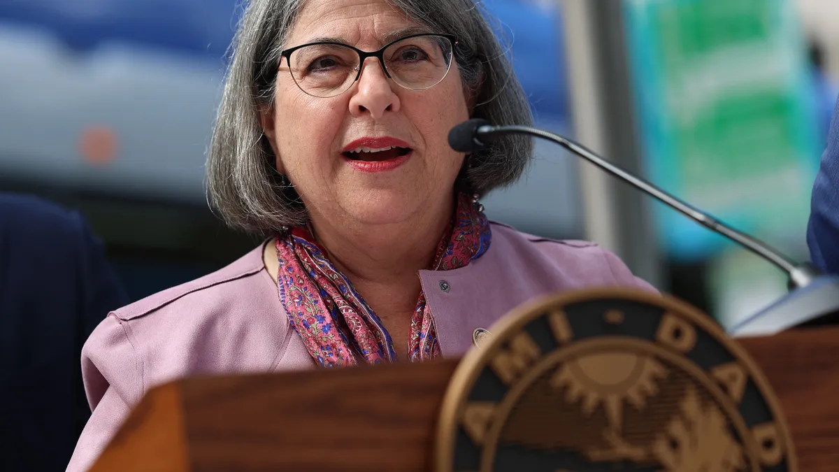 A woman speaks at a lectern with the Miami-Dade County, Florida, insignia on its front.