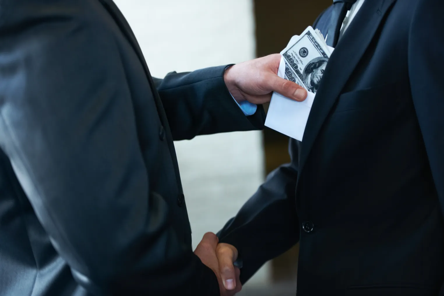 Two corporate businessmen shaking hands while one man places money in the other's pocket.