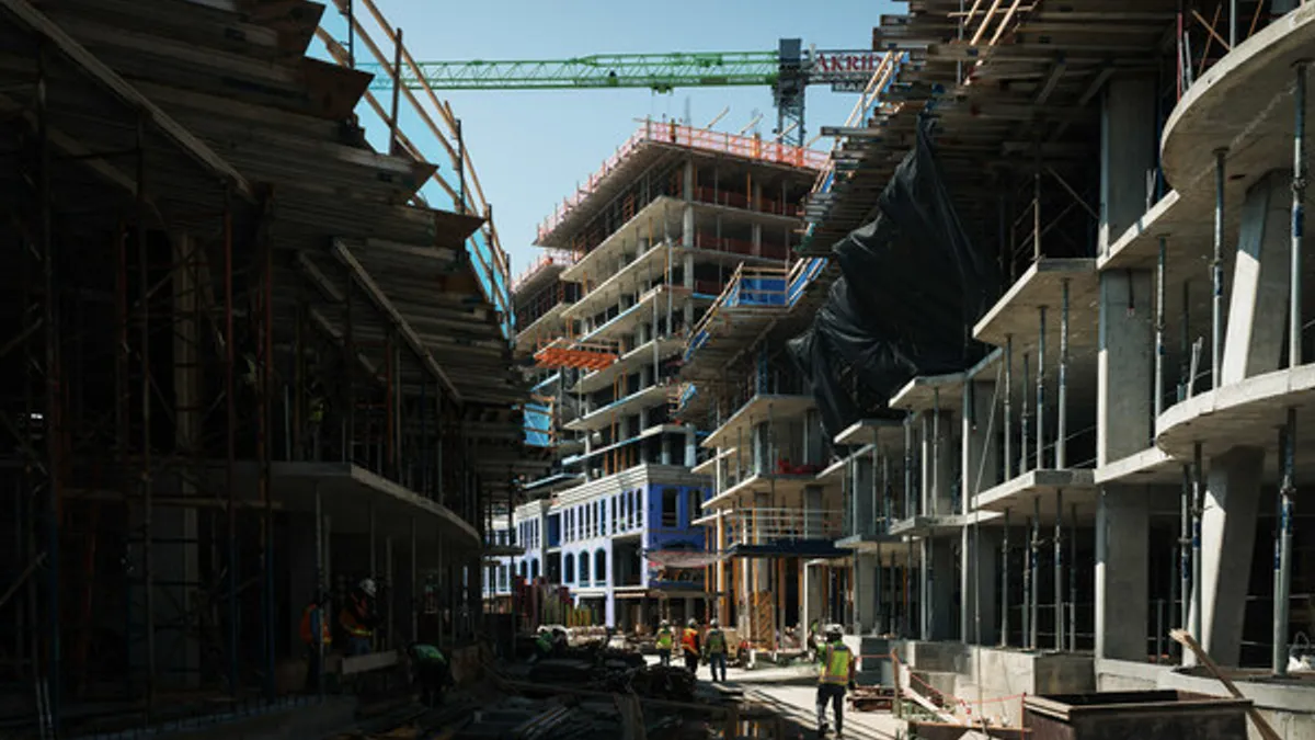 A ground view of several buildings under construction, a crane looms in the background.