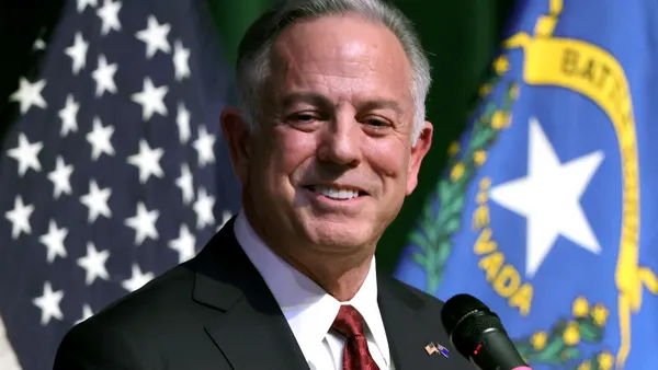 Nevada Gov. Joe Lombardo standing in front of microphone with American and Nevada flags behind him