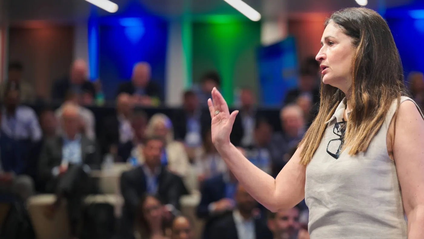 A profile view of a person speaking with numerous blurred audience behind them.