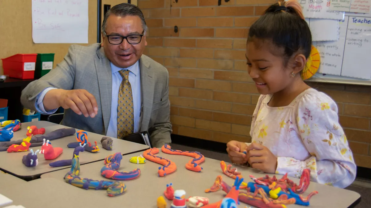 An adult and a young students are sitting at a table. In front of them are figures created with  Play-doh