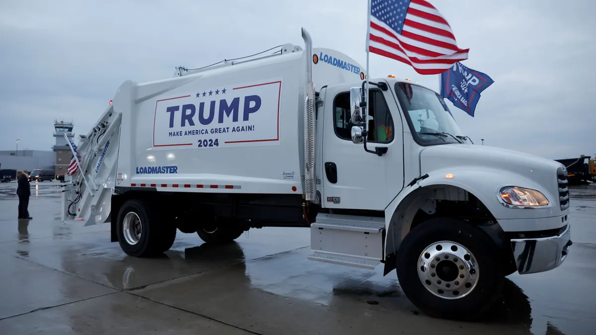 A garbage truck with an American flag attached to the cab is emblazoned with Donald Trump's 2024 campaign logo.