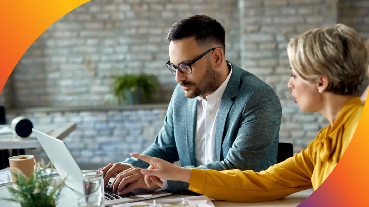 Woman pointing at a laptop while a man types on it in a business meeting