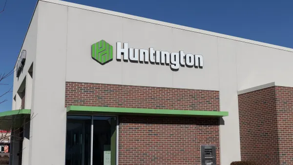 A small, single-story bank building with a red brick and white exterior and a green trim; the sign says "Huntington."