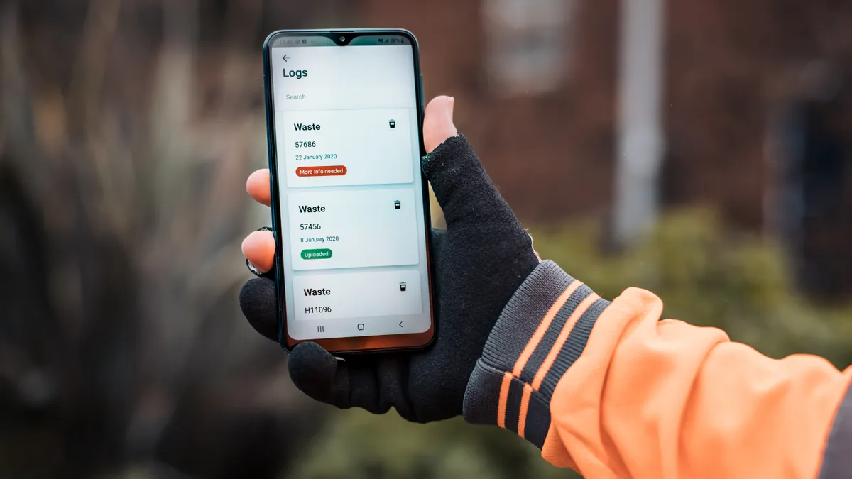 A person wearing thick work gloves holds up a phone with a demonstration of the Qflow app.