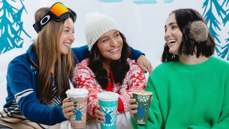 Several consumers hold coffees in front of a wintry background.