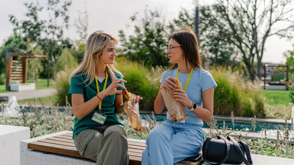 Two young female nurses in scrubs taking a lunch break in the park.