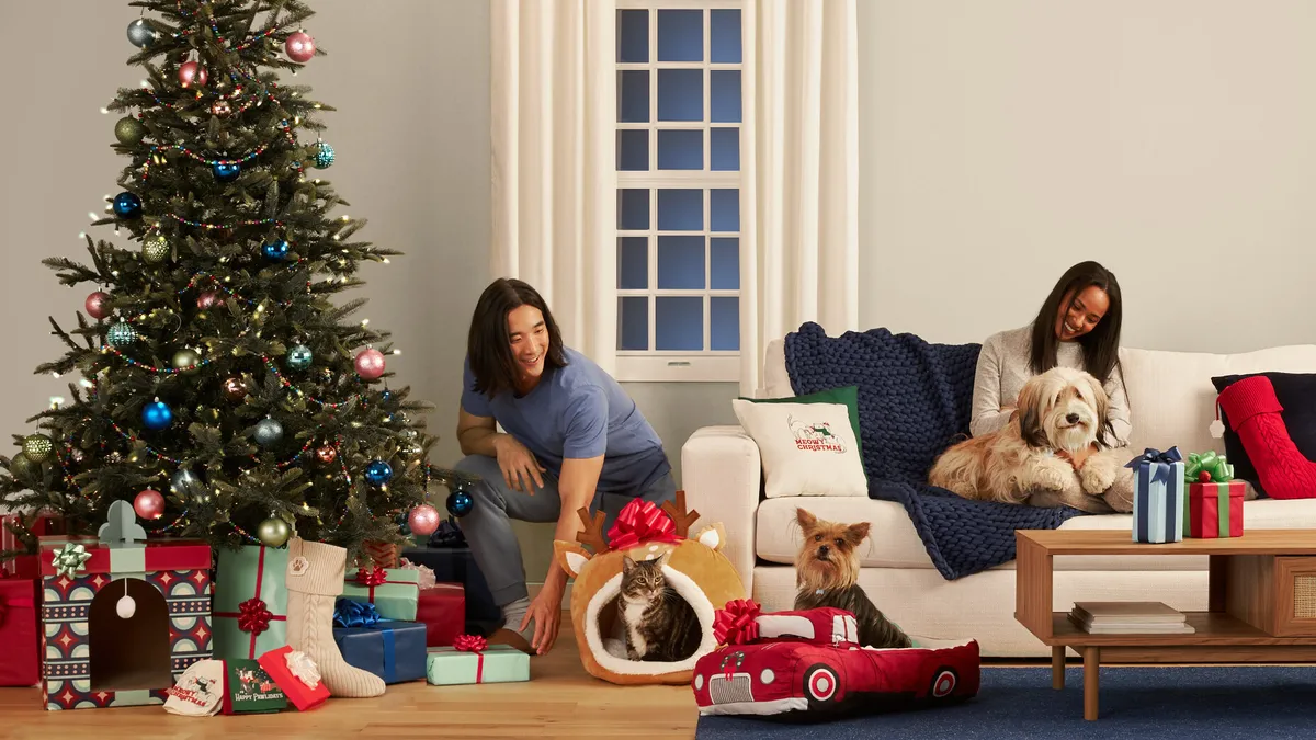 Two people sitting with two dogs and one cat near a Christmas tree.