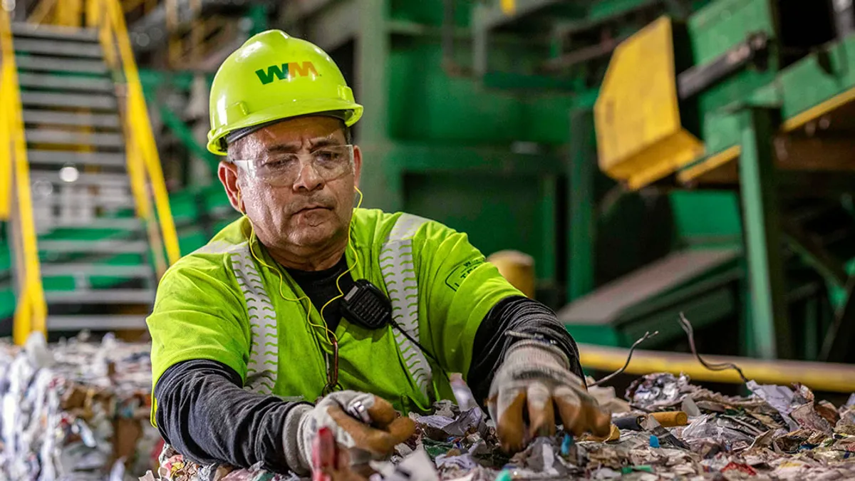 Worker in safety helmet and vest sorts through recyclables on conveyor belt