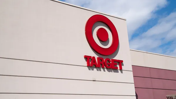 A red bullseye logo with the word Target underneath decorates a storefront against a bright blue sky with puffy white clouds.